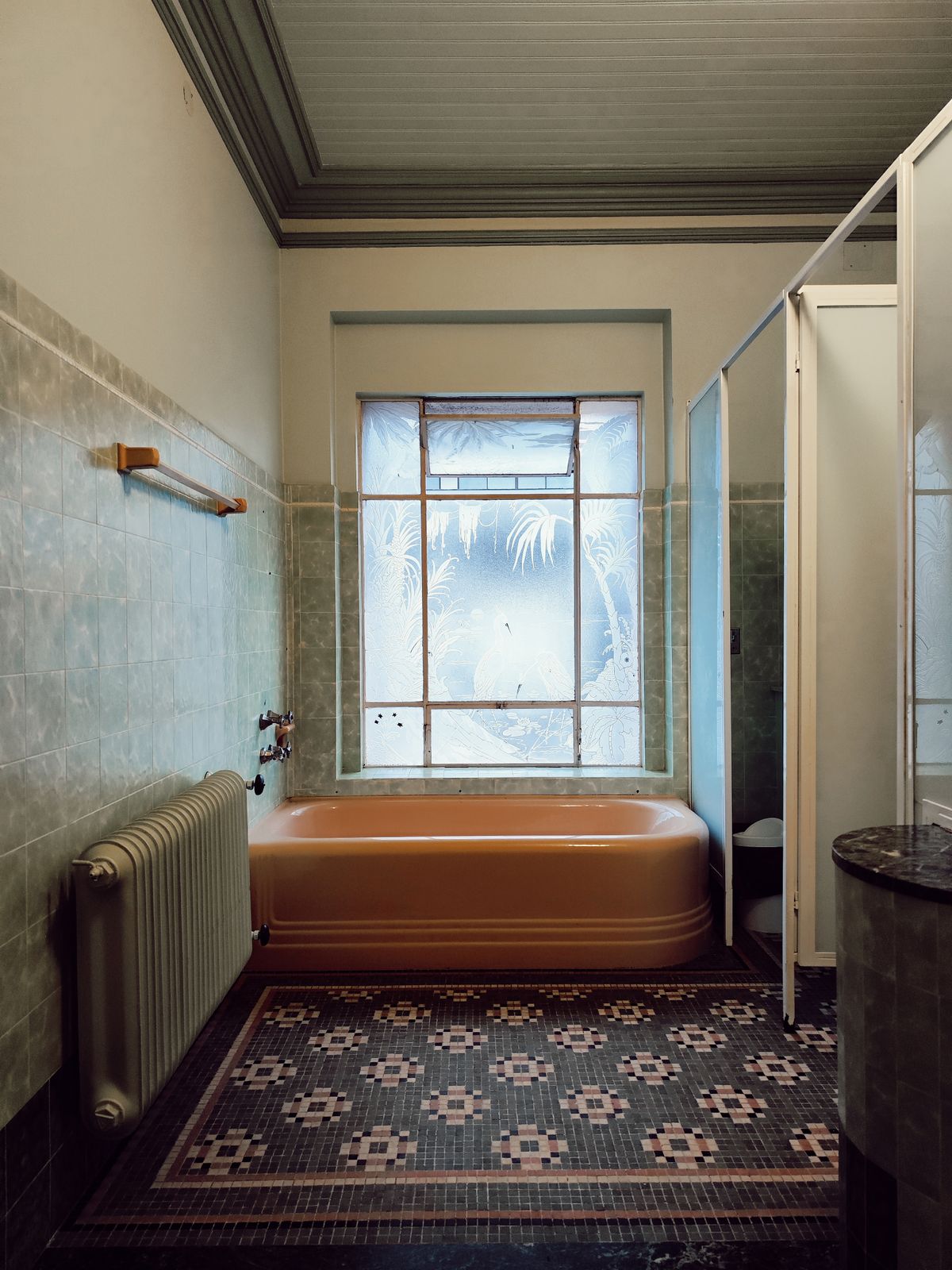 Foto di un bagno anni Sessanta: vasca color salmone, piastrelle verdi, pavimento a mosaico e una grande finestra con vetro decorato.