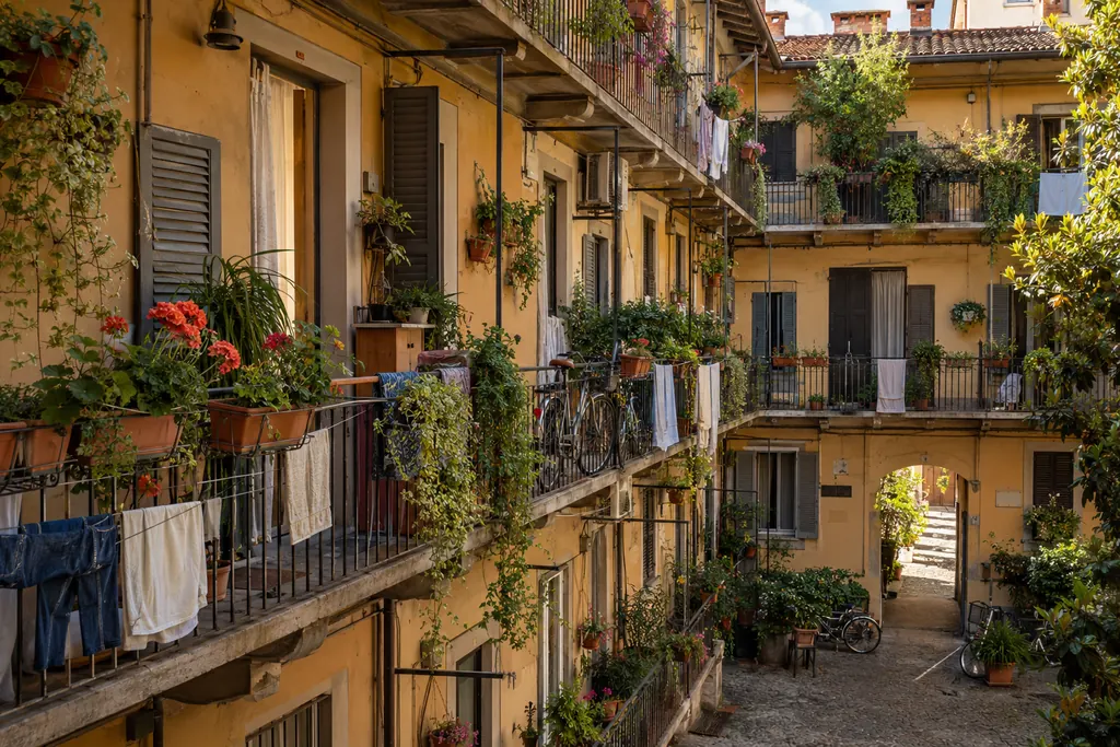 Immagine illustrativa generata con IA: il cortile di una casa di ringhiera milanese con gerani sui ballatoi e biciclette appoggiate al muro.